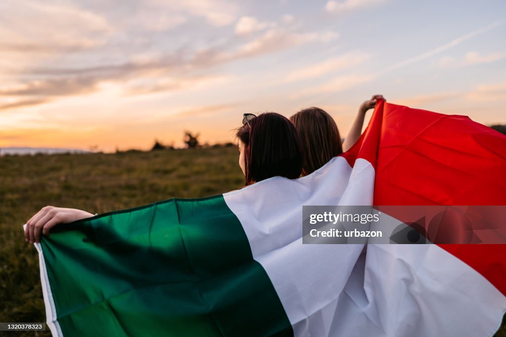 Due donne che si coprono con bandiera italiana sul prato