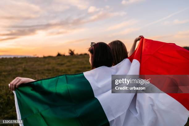 two women  covering themselves with italian flag on meadow - italy flag stock pictures, royalty-free photos & images