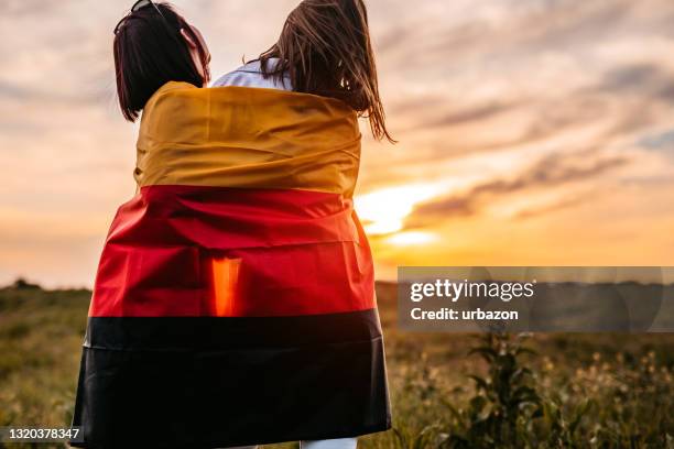 zwei frauen bedecken sich mit deutschlandfahne auf wiese - deutschland flagge stock-fotos und bilder