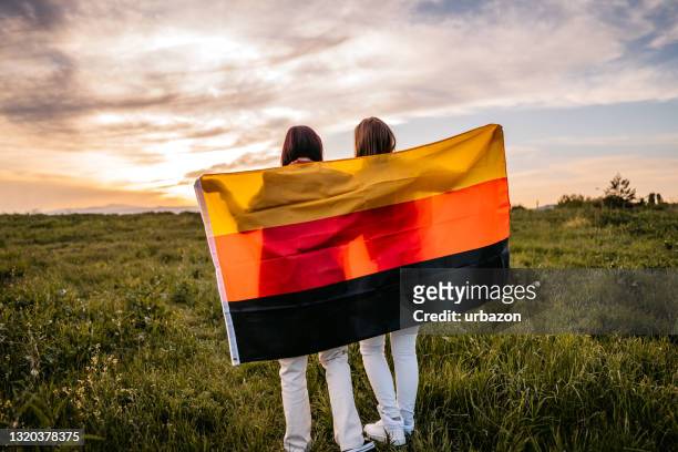 zwei frauen bedecken sich mit deutschlandfahne auf wiese - german culture stock-fotos und bilder