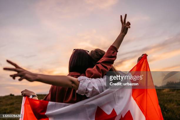 two women  covering themselves with canadian flag on meadow - bandeira do canadá imagens e fotografias de stock