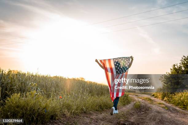 silhouette der frau hält eine amerikanische flagge in ihren händen, über ihrem kopf erhoben. unabhängigkeitstag. rückansicht. im hintergrund sonnenuntergang. - july fourth stock-fotos und bilder