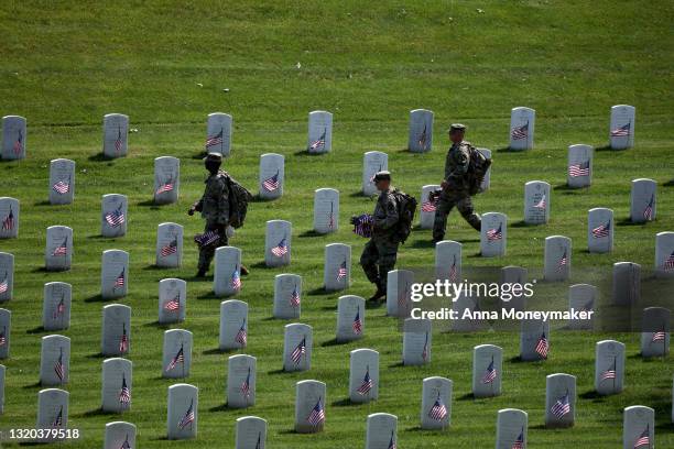 Service members walk through Arlington National Cemetery carrying small American Flags for the “Flags In” ceremony ahead of the Memorial Day weekend...