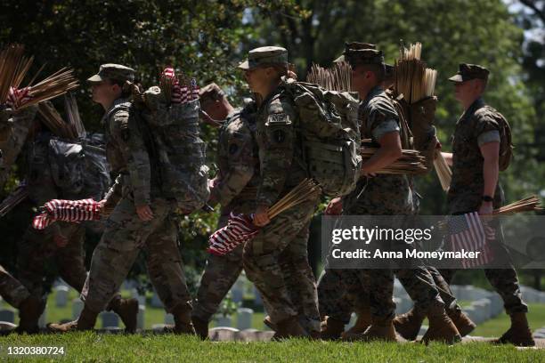 Service members walk through Arlington National Cemetery carrying small American Flags for the “Flags In” ceremony ahead of the Memorial Day weekend...