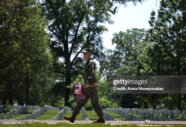 Service member walks through Arlington National Cemetery carrying small American Flags for the “Flags In” ceremony ahead of the Memorial Day weekend...