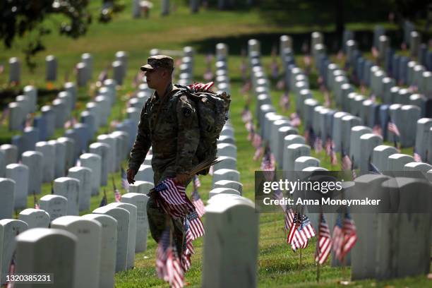 Service member walks through Arlington National Cemetery carrying small American Flags for the “Flags In” ceremony ahead of the Memorial Day weekend...