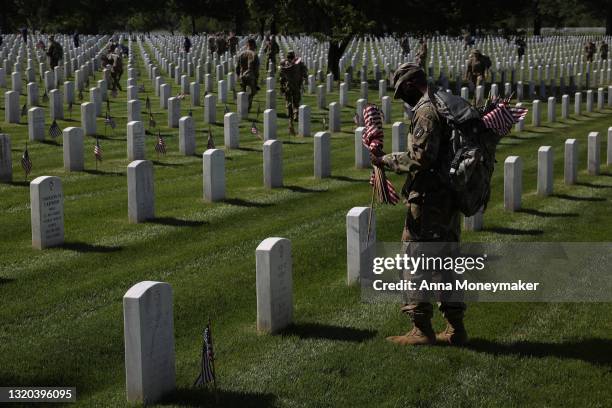 Service members place a small American flag in front of a gravesite as part of the “Flags In” ceremony ahead of the Memorial Day weekend at Arlington...