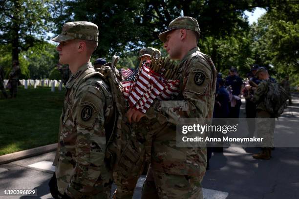 Service members adjust one another's backpacks ahead placing flags in front of gravesites as part of the “Flags In” ceremony ahead of the Memorial...