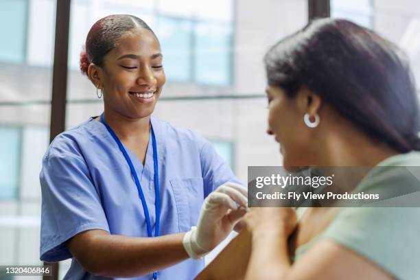 smiling nurse preps patients arm prior to providing flu vaccine - syringe stock pictures, royalty-free photos & images
