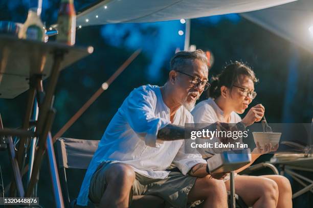 asian chinese senior couple enjoying dinner at camping tent late evening - camping couple stock pictures, royalty-free photos & images