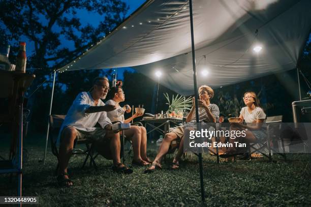 famille chinoise asiatique avec la progéniture de 2 adolescents appréciant le dîner à la tente de camping tard le soir - camping photos et images de collection