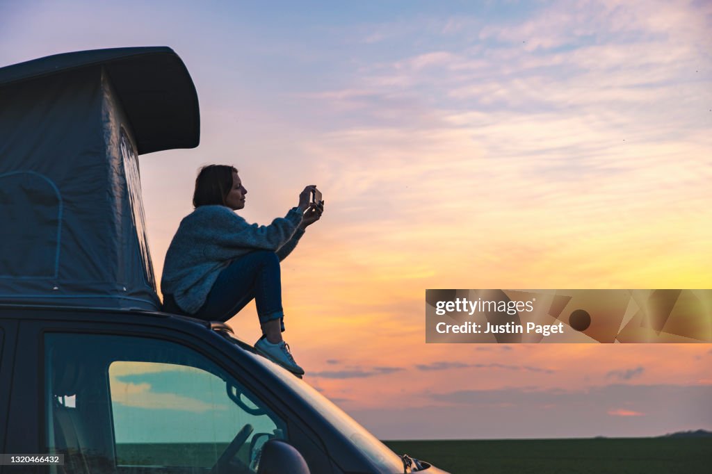 Woman photographing the sunset from the rood of her campervan