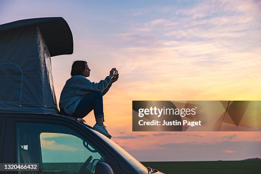 Woman photographing the sunset from the rood of her campervan Woman photographing the sunset from the rood of her campervan