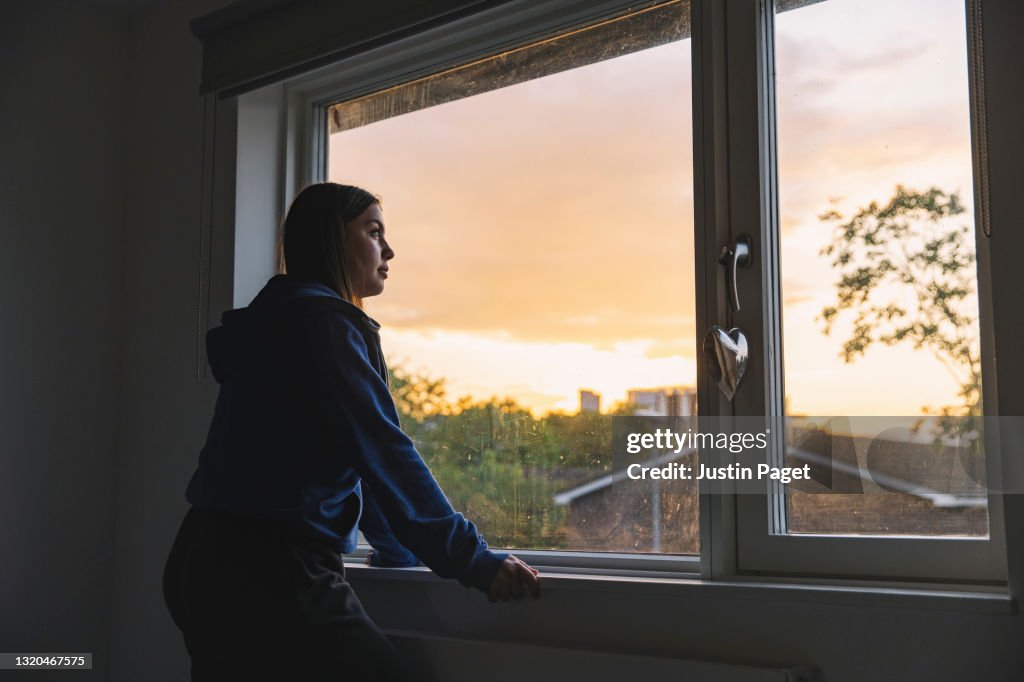 Profile view shot of a teenage girl looking out of her window at sunset