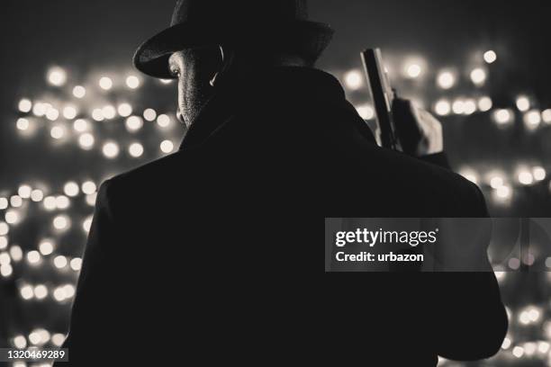 hombre retro con abrigo y sombrero sosteniendo un arma - mafia fotografías e imágenes de stock