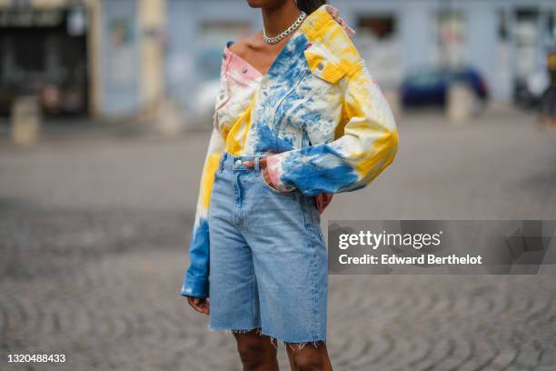 Emilie Joseph @in_fashionwetrust wears a silver chain necklace, black sunglasses, a white yellow blue and orange tie and dye denim jacket by Levis, a...