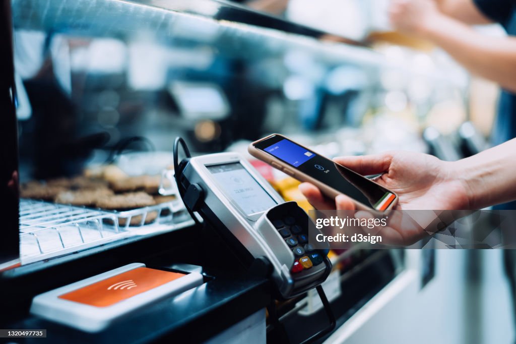 Close up of a woman's hand paying with her smartphone in a cafe, scan and pay a bill on a card machine making a quick and easy contactless payment. NFC technology, tap and go concept
