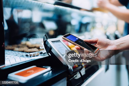 Close up of a woman's hand paying with her smartphone in a cafe, scan and pay a bill on a card machine making a quick and easy contactless payment. NFC technology, tap and go concept Close up of a woman's hand paying with her smartphone in a cafe, scan and pay a bill on a card machine making a quick and easy contactless payment. NFC technology, tap and go concept