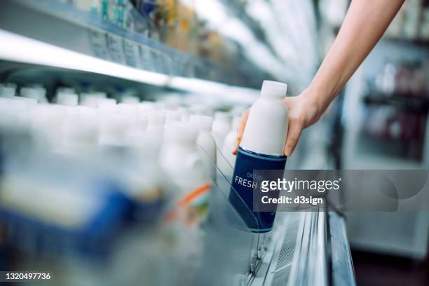close up of a woman's hand picking up a bottle of organic fresh milk from the dairy aisle in supermarket. daily grocery shopping routine. healthy eating lifestyle - milk pack 個照片及圖片檔