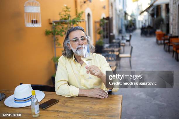 voyageur solo mature assis au café et dégustant du vin blanc pendant la belle journée de printemps à limassol - limassol photos et images de collection