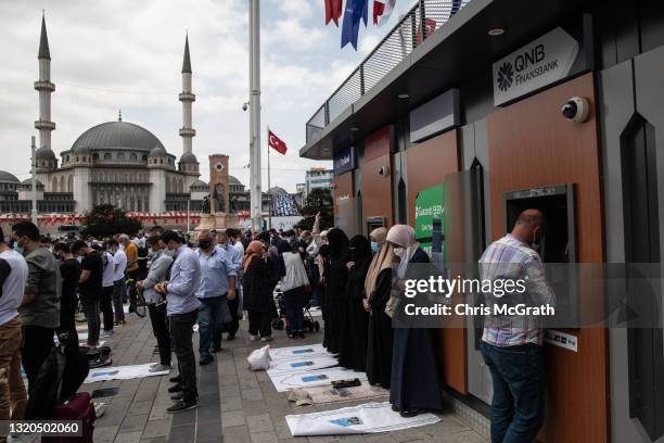 Man uses an ATM machine as women pray during Friday prayers outside the newly completed Taksim Mosque during the opening ceremony at Taksim Square on...