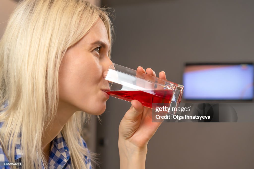 Portrait of a young cute blonde woman who drinks cherry juice from a glass