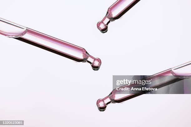 close-up glass pipettes spilling drops of transparent lotion for skin care routine on futuristic gray reflective surface. trendy products of the year - cuentagotas fotografías e imágenes de stock