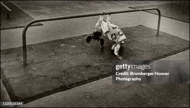 View of a young girl as she hangs from a low balance beam in a school playground, Simi Valley, California, 1976.