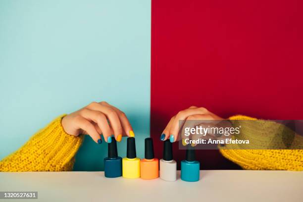 woman hands with manicure and in illuminating yellow knitted sweater are touching five glass bottles with nail polish placed on white table against background divided on two parts: light blue and red. trendy colors of the year 2021 - マニキュア ストックフォトと画像