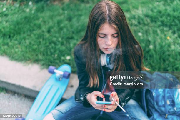 schoolgirl smoking cigarette in the park and texting - beautiful women smoking cigarettes stock pictures, royalty-free photos & images