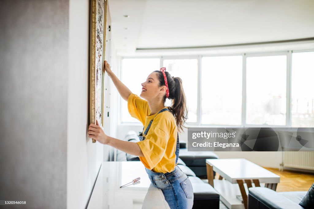 Junge Frau hängt ein Bild an einer Wand mit einem Blick der Konzentration