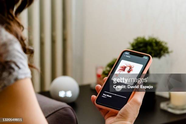 woman choosing music on her cell phone to listen to on her smart speaker - podcasting stock-fotos und bilder