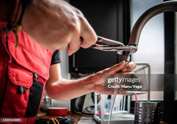 repairman using adjustable pliers to fix kitchen faucet - arreglar fotografías e imágenes de stock