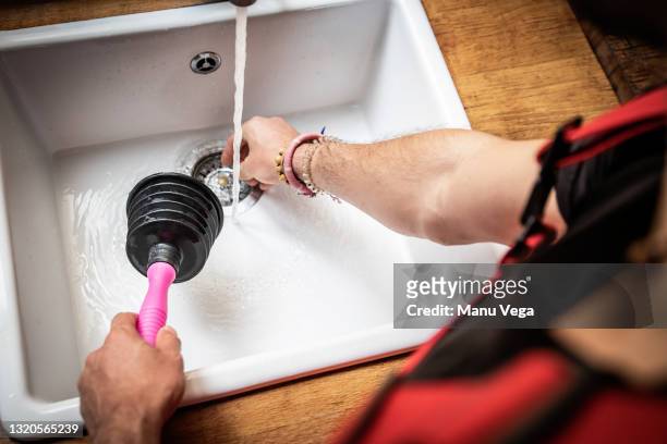 plumber using a pipe plunger to fix kitchen sinks - gootsteen stockfoto's en -beelden