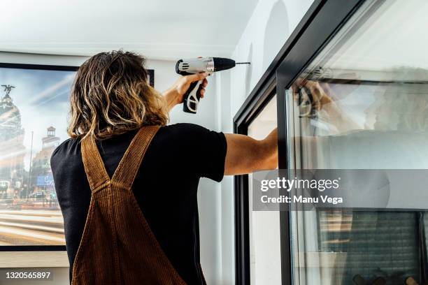 side view of a handyman using electric screwdriver to install curtains in living room - installieren stock-fotos und bilder