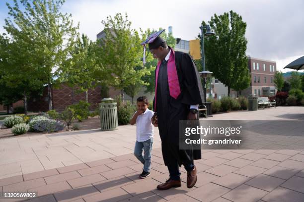 male african american college graduate walking mit seinem dreijährigen sohn am abschlusstag an einer universität - 40 year old black man stock-fotos und bilder