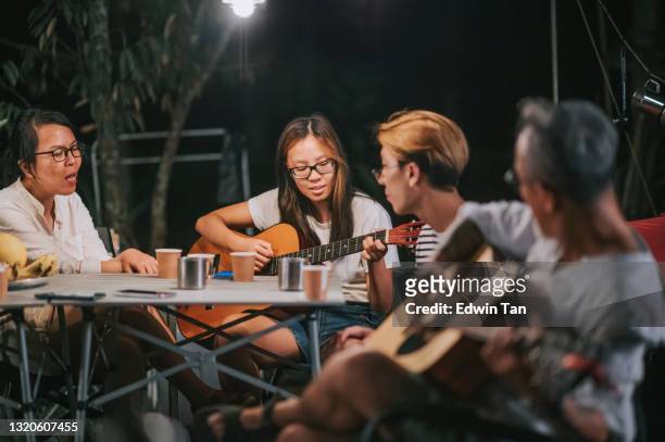 asiatisk kinesisk familj med 2 tonårsavkommor läser mobilapp lyrisk njuta av att spela musikinstrument trädgårdsfest samla camping tält på natten - sm party bildbanksfoton och bilder