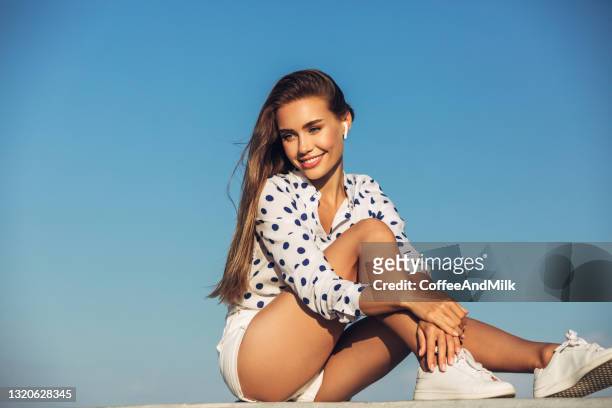 beautiful girl on the beach listening music - woman shorts stock pictures, royalty-free photos & images