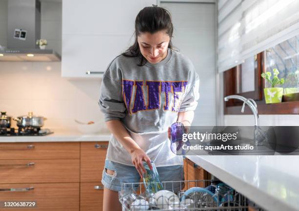 young woman is putting dishes into dishwasher in kitchen. - loading dishwasher stock pictures, royalty-free photos & images