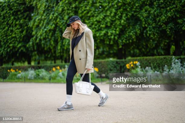 Xenia Adonts wears a black cap from Museum of Peace and Quiet, a black ribbed turtleneck pullover, a beige long oversized jacket from Attire The...