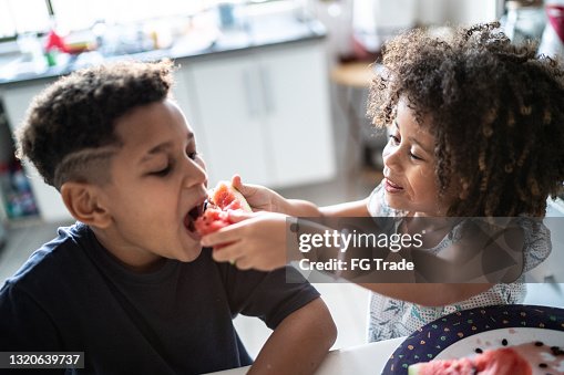 Girl feeding brother with slice of watermelon at home