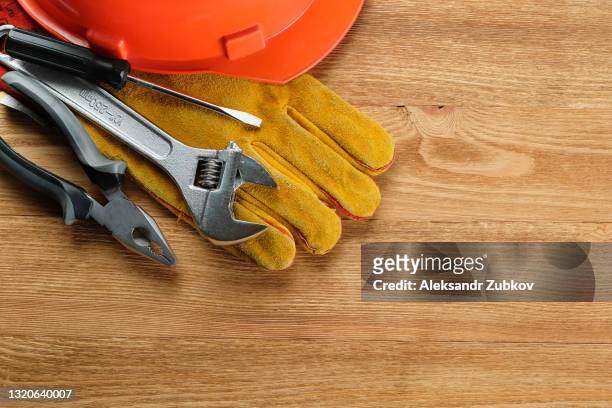 tools for building a house or repairing an apartment, on a wooden background or table. workplace of the foreman. the topic of home and professional repairs, business and construction industry. protective gloves, hard hat, pliers, screwdriver and wrench. - hand tool foto e immagini stock