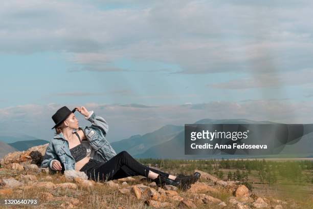 a young graceful girl dressed in a black hat with wide brim walks among the mountains. a clear sunny day in the altai mountains. a tourist trip to the depths of russian nature, high mountain ranges. - hot young model stock pictures, royalty-free photos & images