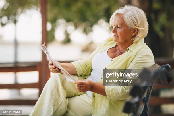 lovely senior woman is sitting on bench in park, reading newspapers. - the weekend in news around the world stock pictures, royalty-free photos & images