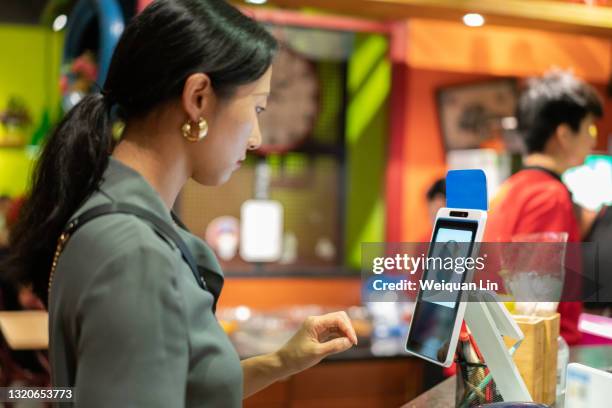 young attractive asian woman is using facial recognition technology to pay - biometrie stock-fotos und bilder