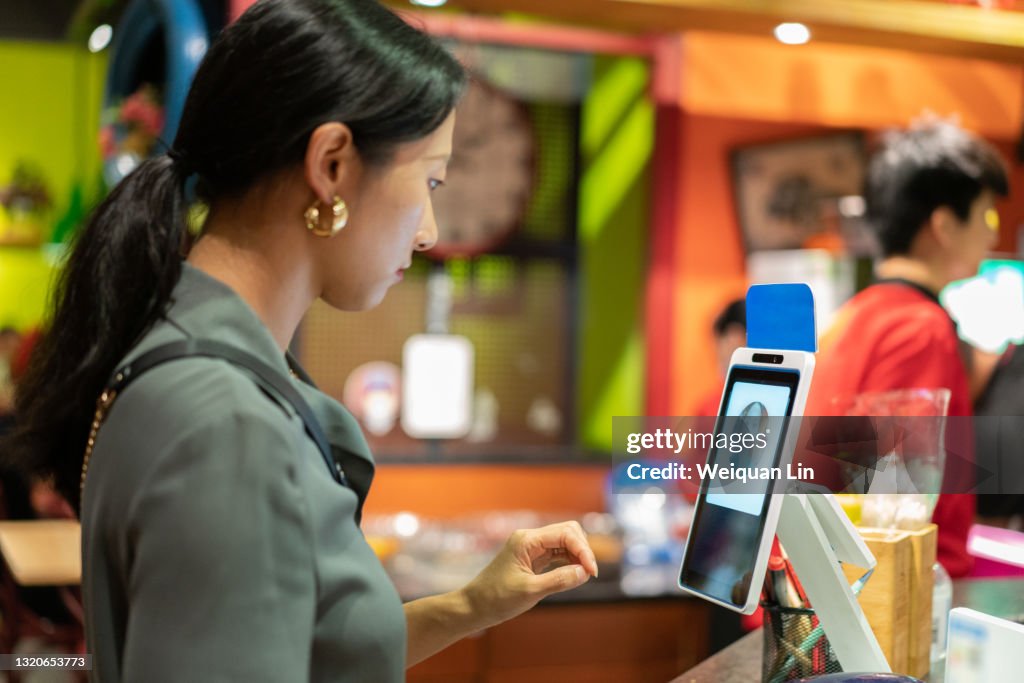 Young attractive Asian woman is using facial recognition technology to pay