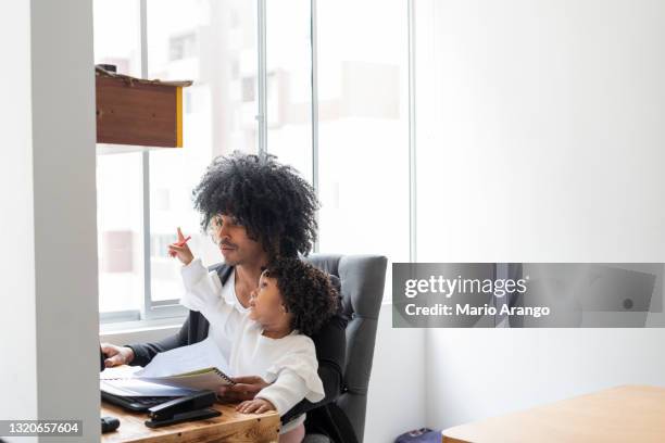 young black father with his latino daughter both sitting at the workplace while the father looking to finish his work and his daughter distracts him by playing - distracts stock pictures, royalty-free photos & images