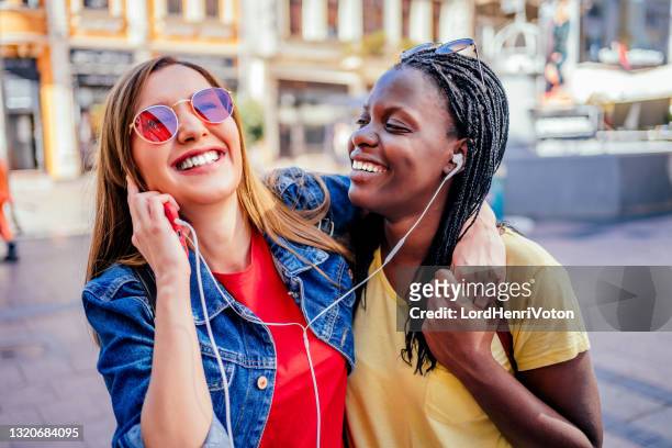 young female friends listening music together - sharing headphones stock pictures, royalty-free photos & images