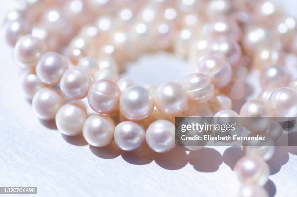 close-up of a pink colored pearl necklace, coiled around itself on a silver background - perla fotografías e imágenes de stock