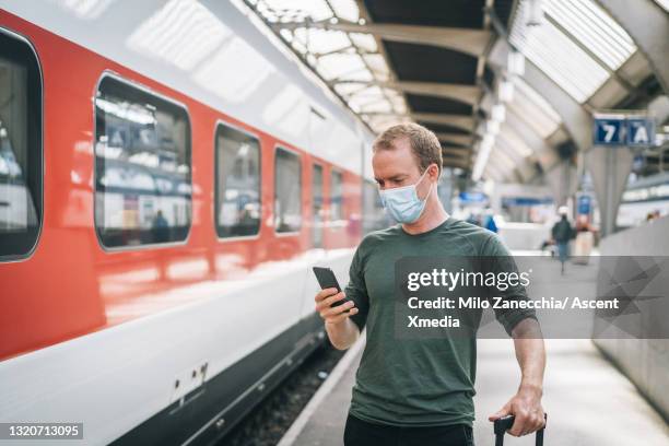 young man waits for train at swiss train station - face mask with handle stock-fotos und bilder